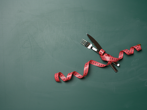 fork and knife wrapped in green measuring tape on a green background, weight loss concept, flat lay