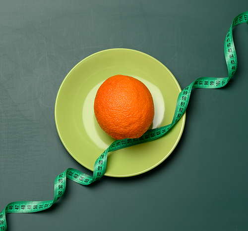 orange wrapped in green measuring tape on a round plate, slimming concept, cellulite, top view