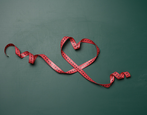 red heart shaped measuring tape on green chalkboard, top view