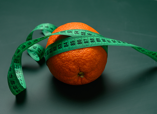 orange wrapped in green measuring tape, slimming concept, cellulite, close up