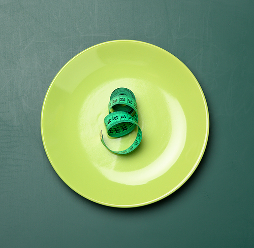 green round plate and green measuring tape on a green background, weight loss concept, flat lay