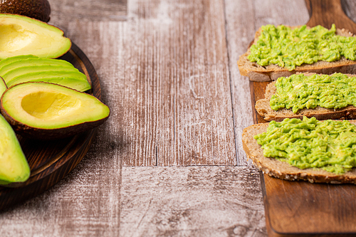 Avocado sandwiches next to cutted ones on wooden board.