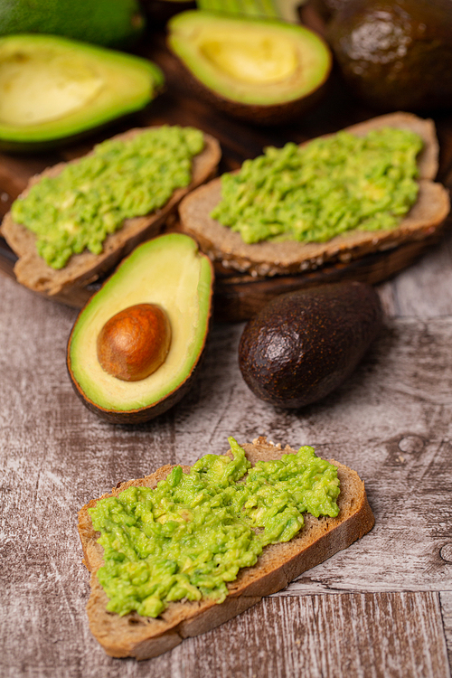 Avocado sandwiches next to cutted ones on wooden board.