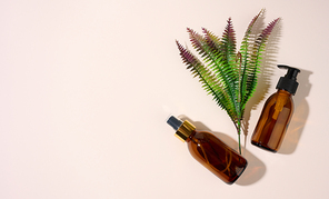 brown glass bottles with dispenser and a sprig of fern on a beige background. Packaging for gel, serum, advertising and promotion. Natural organic products. Mock up