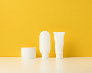 jar, bottle and empty white plastic tubes for cosmetics on a yellow background. Packaging for cream, gel, serum, advertising and product promotion, mock up