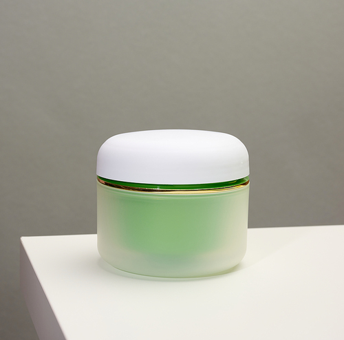 green jar for cosmetics on a white table. Packaging for cream, gel, serum, advertising and product promotion, mock up