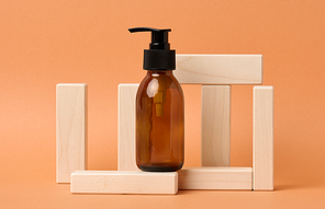 Brown glass bottle with black pump of cosmetic products on wooden block on a orange paper background. Natural organic spa cosmetic, beauty concept. Mockup