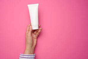 female hand holding white plastic tube. Packaging for cream, gel, serum, advertising and product promotion