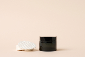 cosmetic products in a black glass jar with a lid and white cotton pad. Blank for branding products, moisturizer on beige background