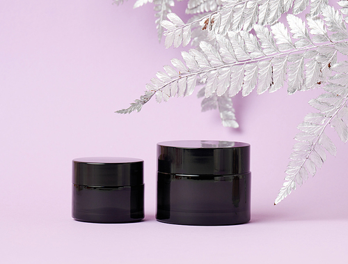 black glass jar for cosmetics on a purple background. Packaging for cream, gel, serum, advertising and product promotion, mock up