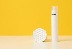 cosmetic products in a white plastic bottle and white cotton pad. Blank for branding products, moisturizer on yellow background