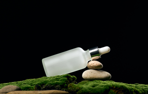 white glass bottle with pipette stands on green moss, black background. Cosmetics SPA branding. Packaging for gel, serum, advertising and product promotion, mock up