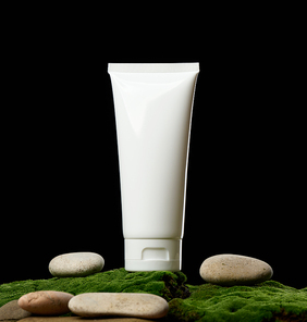 empty white plastic tubes for cosmetics stands on green moss, black background. Packaging for cream, gel, serum, advertising and product promotion, mock up