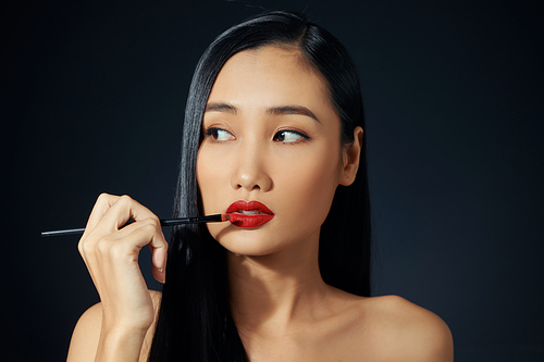 Closeup portrait of beautiful young woman with makeup brushes. Red lips. Isolated over blachbackground.