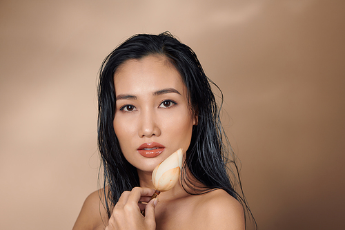 Attractive long-haired girl smiling and holding dried lotus buds on beige background.