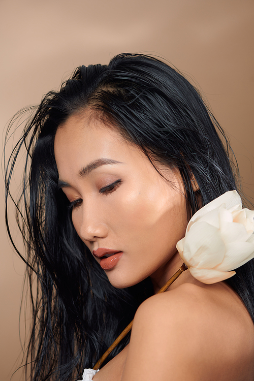 Beautiful young asian girl with natural make-up and wet hair posing in the studio on a beige background