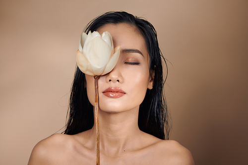 Beautiful young asian girl with natural make-up and wet hair posing in the studio on a beige background