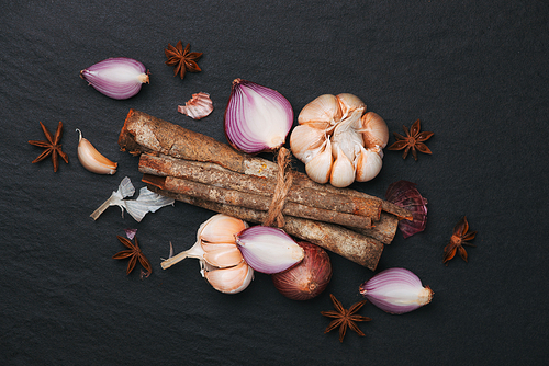 Cooking ingredients: cinnamon sticks and garlic on black stone table.