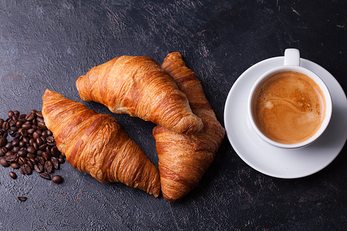 Croissants with mug of coffee and coffee beans on dark wooden table. Delicious desserts