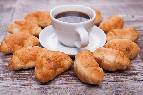 Freshly baked croissants on rustic wooden table with cup of coffee. Delicious coffee.