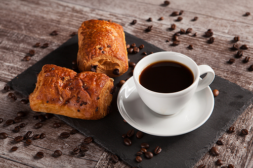 Sweet Croissants with almonds, hot coffee and spreaded coffee beans. Sweet breakfast.