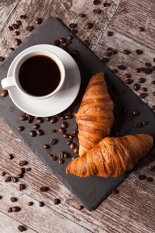 Cup of coffee and spreaded coffee beans with fresh croissants. Delicous dessert.