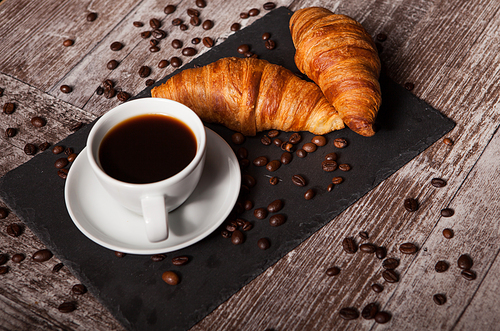 Croissant and cup of hot coffee on dark wooden table. Great breakfast.