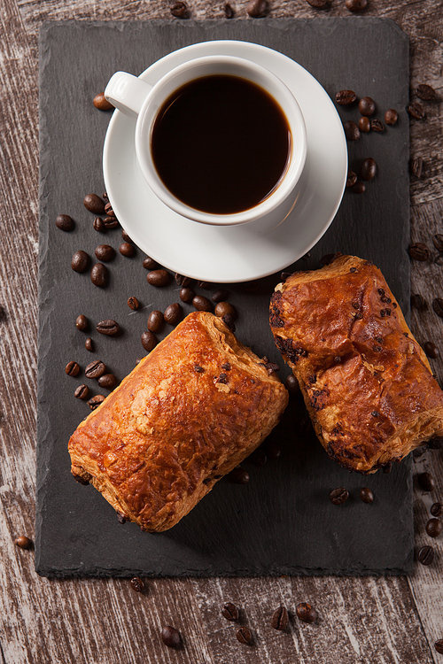 Mug of coffee with delicious pastry and spreaded beans of coffee. Fresly baked.