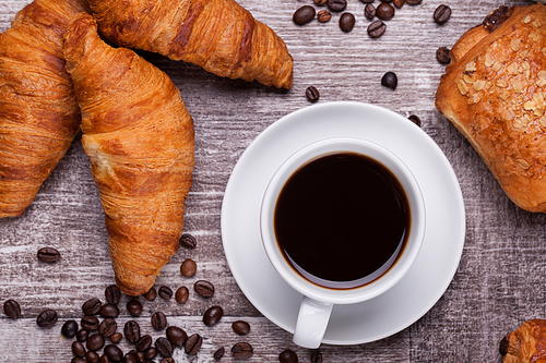 Cup of hot coffee and freshly baked croissants on dark wooden table. Tasty croissant.