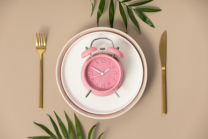 Composition with cutlery, plate and alarm clock on color background, flat lay, top view