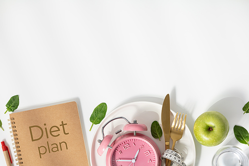 Composition with cutlery, plate, measuring tape, paper notebook and alarm clock on white background, flat lay, top view, copy space