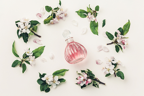 Beautiful perfume bottles and spring flowers on off white background, flat lay, top view