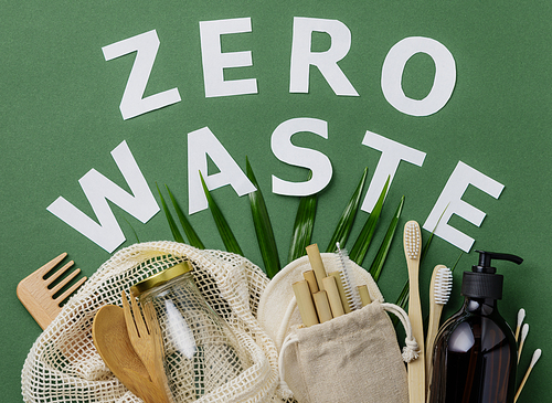 Zero waste concept. Cotton bag, bamboo cultery, glass jar, bamboo toothbrushes, hairbrush and straws on green background with handmade paper letters, flat lay, paper text , copyspace. Plastic free. Sustainable lifestyle concept.