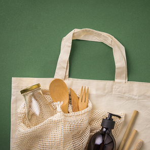 Zero waste concept. Cotton bag, bamboo cultery, glass jar, bamboo toothbrushes, hairbrush and straws on green background, flat lay, paper text , copyspace. Plastic free. Sustainable lifestyle concept.