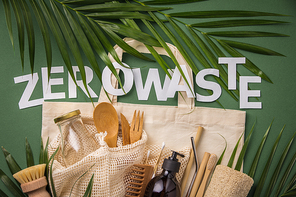 Zero waste concept. Cotton bag, bamboo cultery, glass jar, bamboo toothbrushes, hairbrush and straws on green background with handmade paper letters, flat lay, paper text , copyspace. Plastic free. Sustainable lifestyle concept.