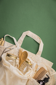 Zero waste concept. Cotton bag, bamboo cultery, glass jar, bamboo toothbrushes, hairbrush and straws on green background, flat lay, paper text , copyspace. Plastic free. Sustainable lifestyle concept.