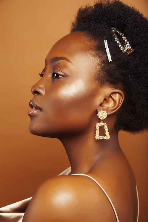 young pretty african model with golden jewelry in fashion style dress smiling happy on brown backround, lifestyle people concept close up