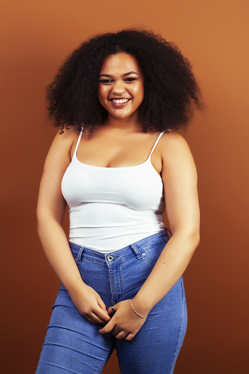 pretty young african american woman with curly hair posing cheerful gesturing on brown background, lifestyle people concept closeup