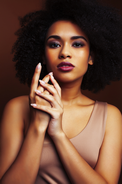 pretty young african american woman with curly hair posing cheerful gesturing on brown background, lifestyle people concept closeup