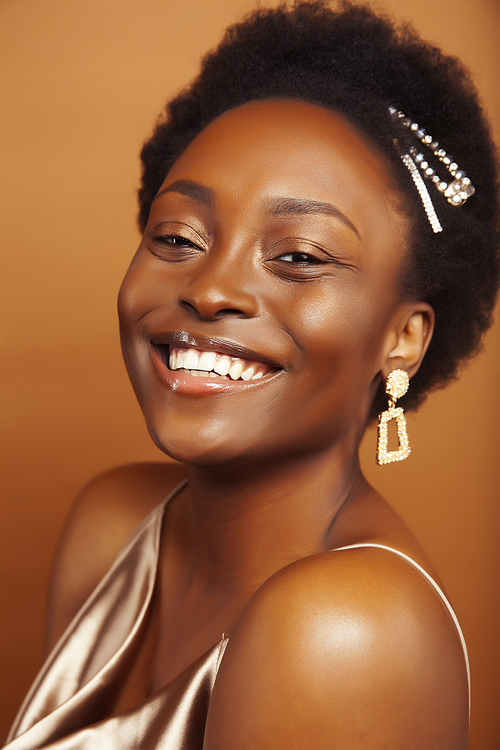 young pretty african model with golden jewelry in fashion style dress smiling happy on brown backround, lifestyle people concept close up