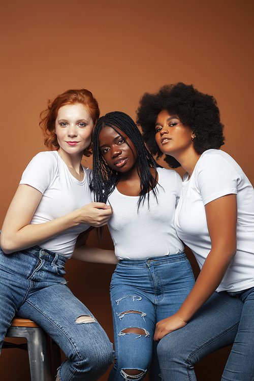 young pretty caucasian, afro, scandinavian woman posing cheerful together on brown background, lifestyle diverse nationality people concept closeup