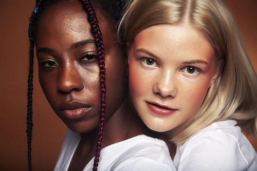 two pretty girls african and caucasian blond posing cheerful together on brown background, ethnicity diverse lifestyle people concept close up