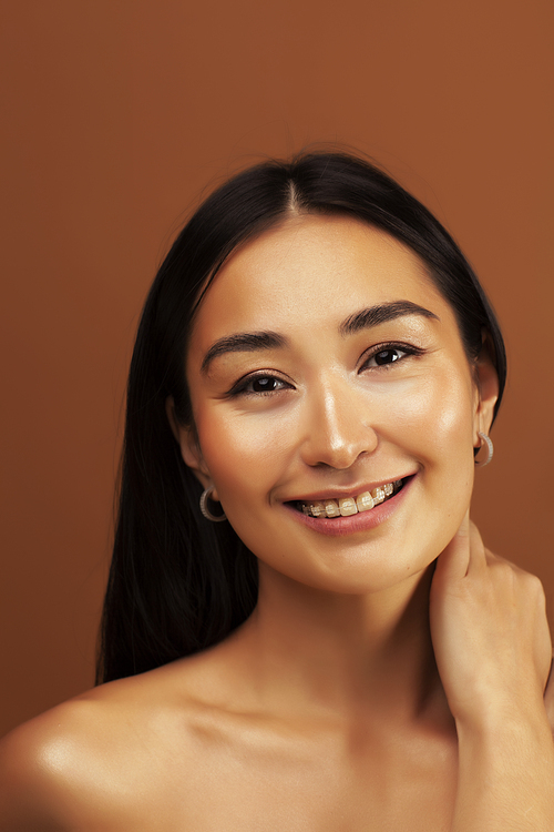 young pretty asian woman cheerful smiling posing on warm brown background, lifestyle people concept closeup