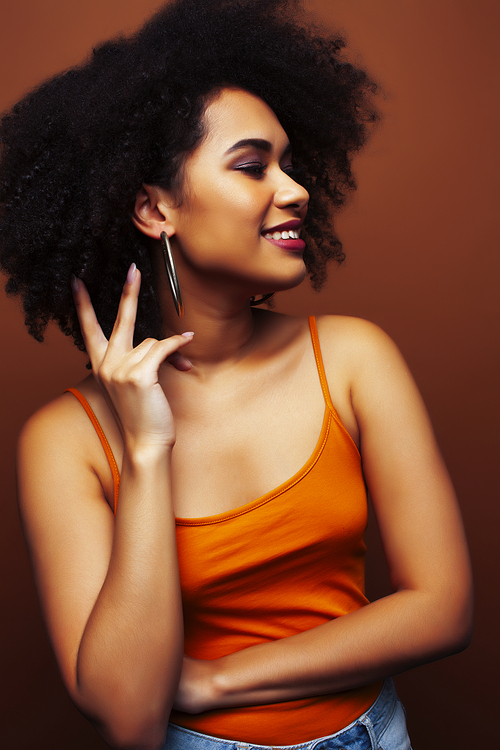 pretty young african american woman with curly hair posing cheerful gesturing on brown background, lifestyle people concept closeup