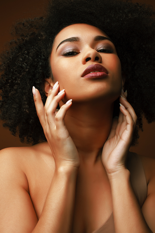 pretty young african american woman with curly hair posing cheerful gesturing on brown background, lifestyle people concept closeup