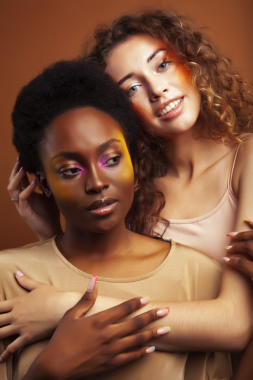 two pretty girls african and caucasian blond posing cheerful together on brown background, ethnicity diverse lifestyle people concept close up