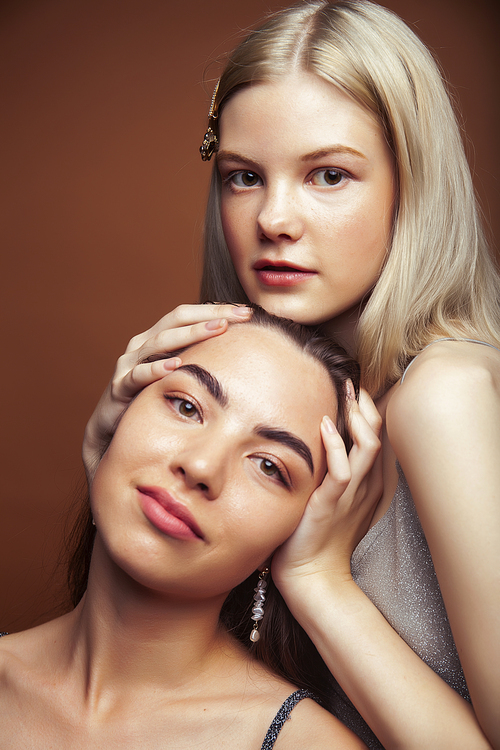 two pretty diverse girls happy posing together: blond and brunette on brown background, lifestyle people concept closeup