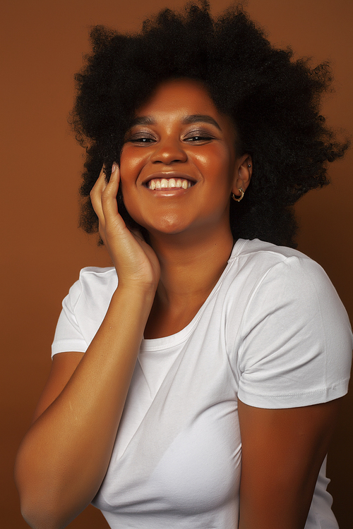 pretty young african american woman with curly hair posing cheerful gesturing on brown background, lifestyle people concept close up