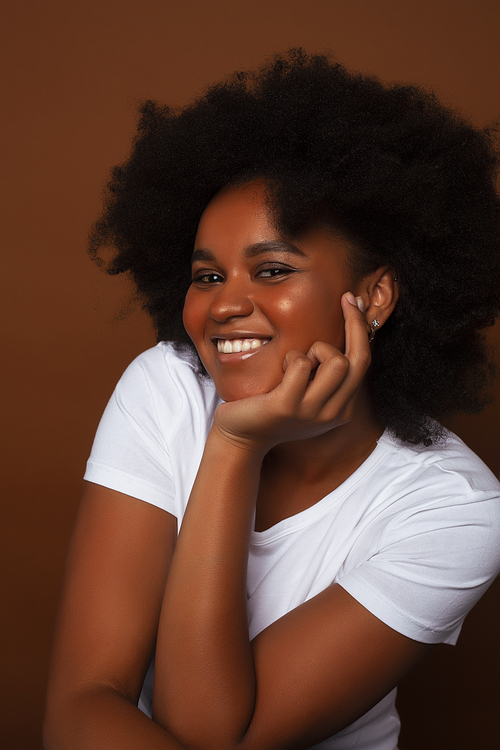 pretty young african american woman with curly hair posing cheerful gesturing on brown background, lifestyle people concept closeup