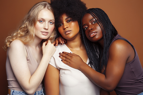 young pretty caucasian, afro, scandinavian woman posing cheerful together on brown background, lifestyle diverse nationality people concept close up